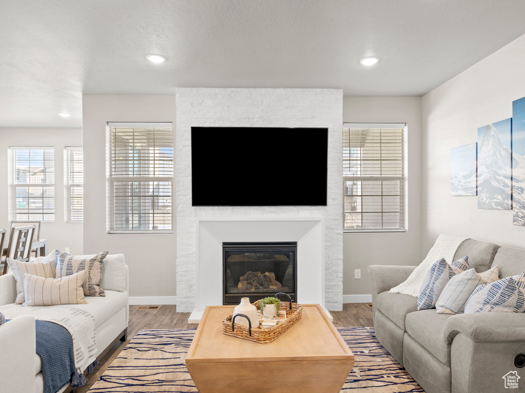 Living room with wood finished floors, a large fireplace, and recessed lighting