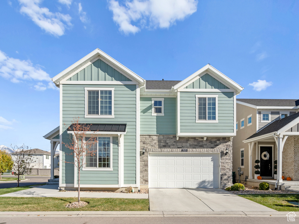 View of front facade featuring board and batten siding, stone siding, driveway, and a garage