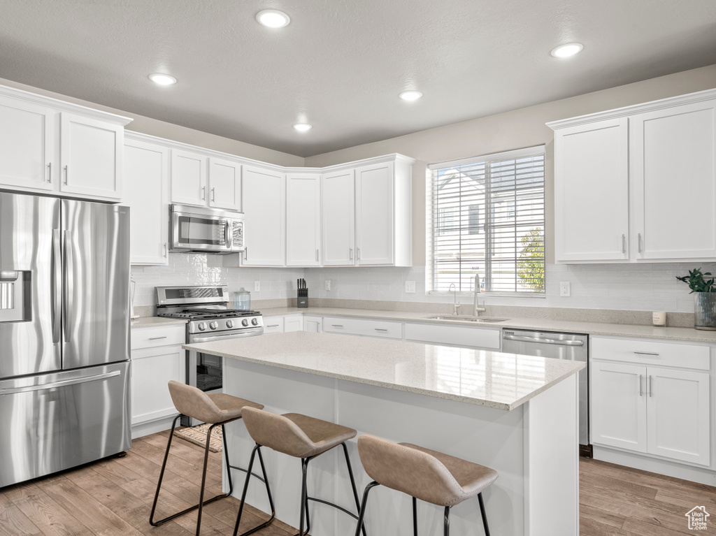 Kitchen featuring stainless steel appliances, a breakfast bar area, white cabinetry, light wood-style flooring, and recessed lighting