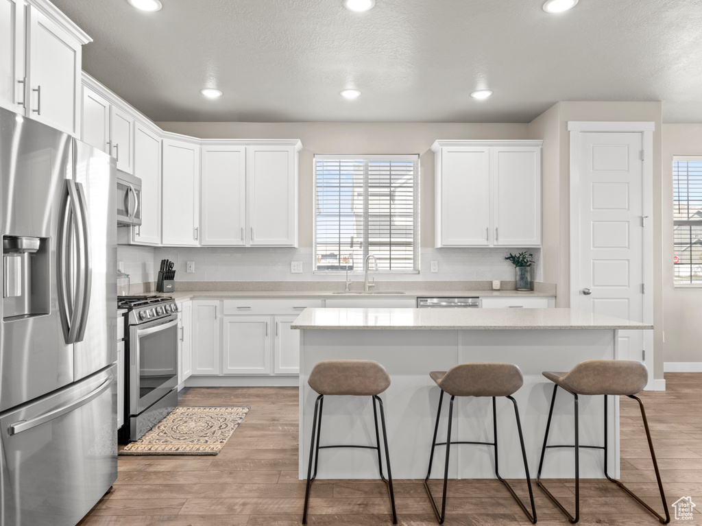 Kitchen with stainless steel appliances, a kitchen bar, white cabinets, a kitchen island, and recessed lighting