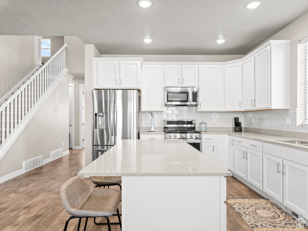 Kitchen with appliances with stainless steel finishes, a center island, a kitchen bar, backsplash, and light wood-type flooring