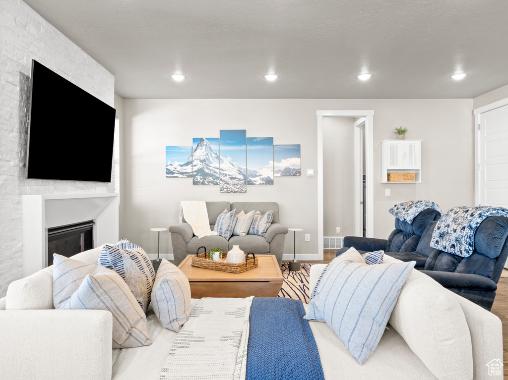 Living area with a glass covered fireplace, wood finished floors, and recessed lighting