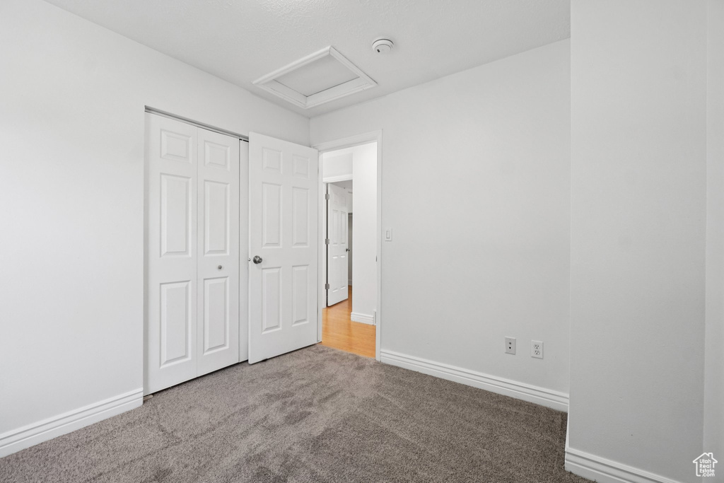 Unfurnished bedroom featuring attic access, carpet flooring, and a closet