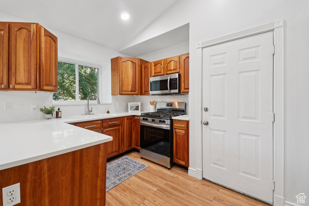 Kitchen featuring stainless steel appliances, brown cabinetry, light wood-style flooring, lofted ceiling, and light countertops