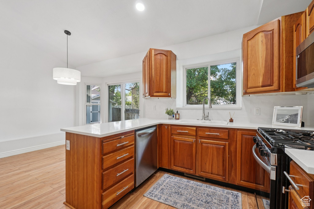 Kitchen featuring stainless steel appliances, a peninsula, backsplash, light countertops, and brown cabinetry