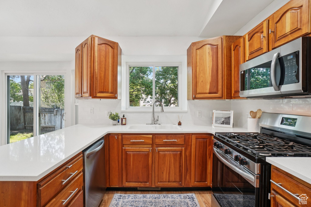 Kitchen with stainless steel appliances, a peninsula, plenty of natural light, and brown cabinetry