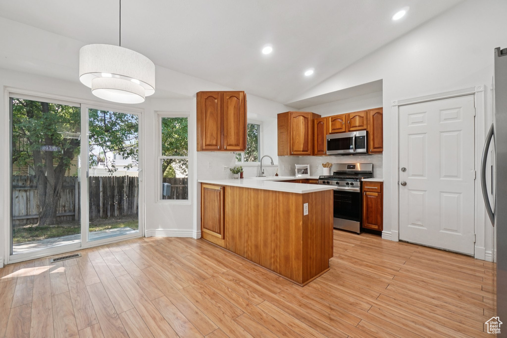 Kitchen with stainless steel appliances, a peninsula, lofted ceiling, brown cabinets, and light countertops