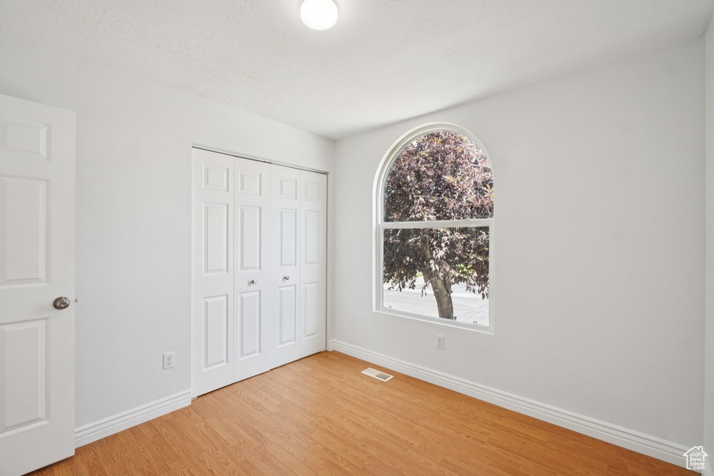 Unfurnished bedroom featuring multiple windows, light wood-style flooring, and a closet