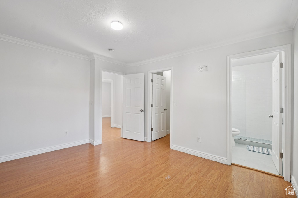 Unfurnished bedroom featuring light wood-style floors, crown molding, a spacious closet, and connected bathroom