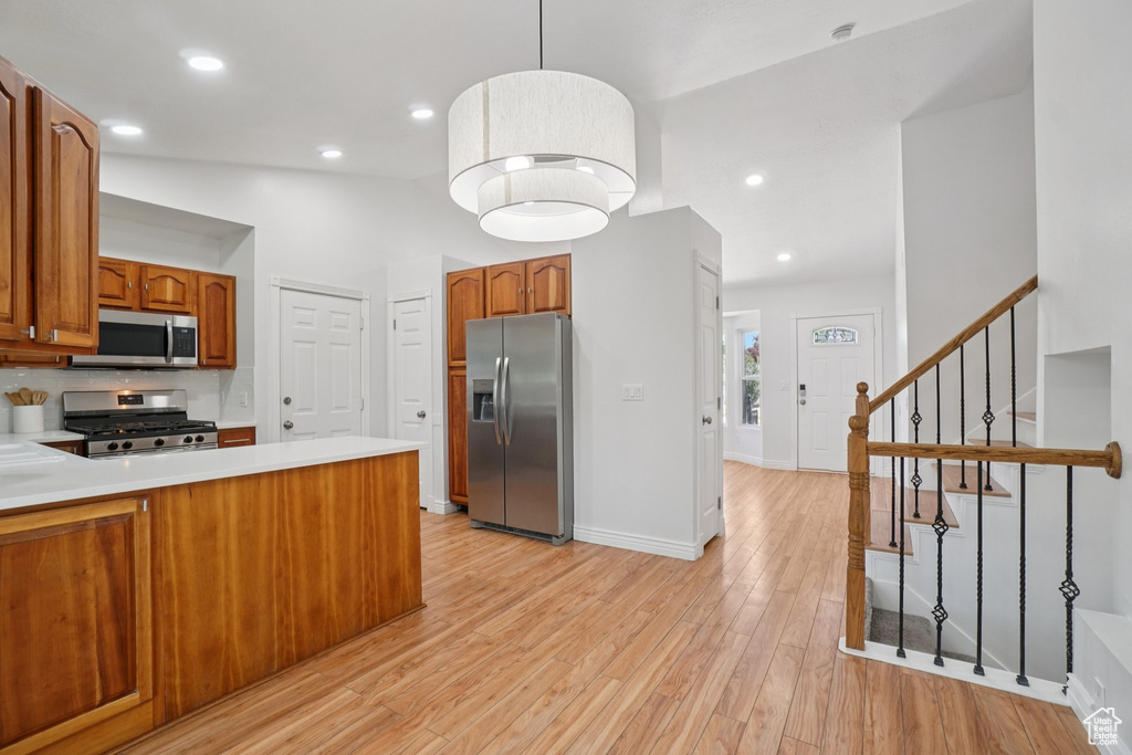 Kitchen with appliances with stainless steel finishes, brown cabinetry, light countertops, light wood finished floors, and recessed lighting