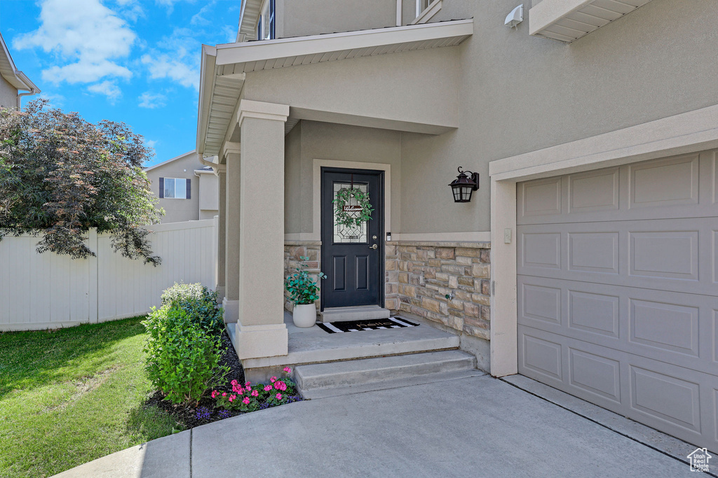 View of exterior entry featuring stone siding, stucco siding, driveway, and a garage