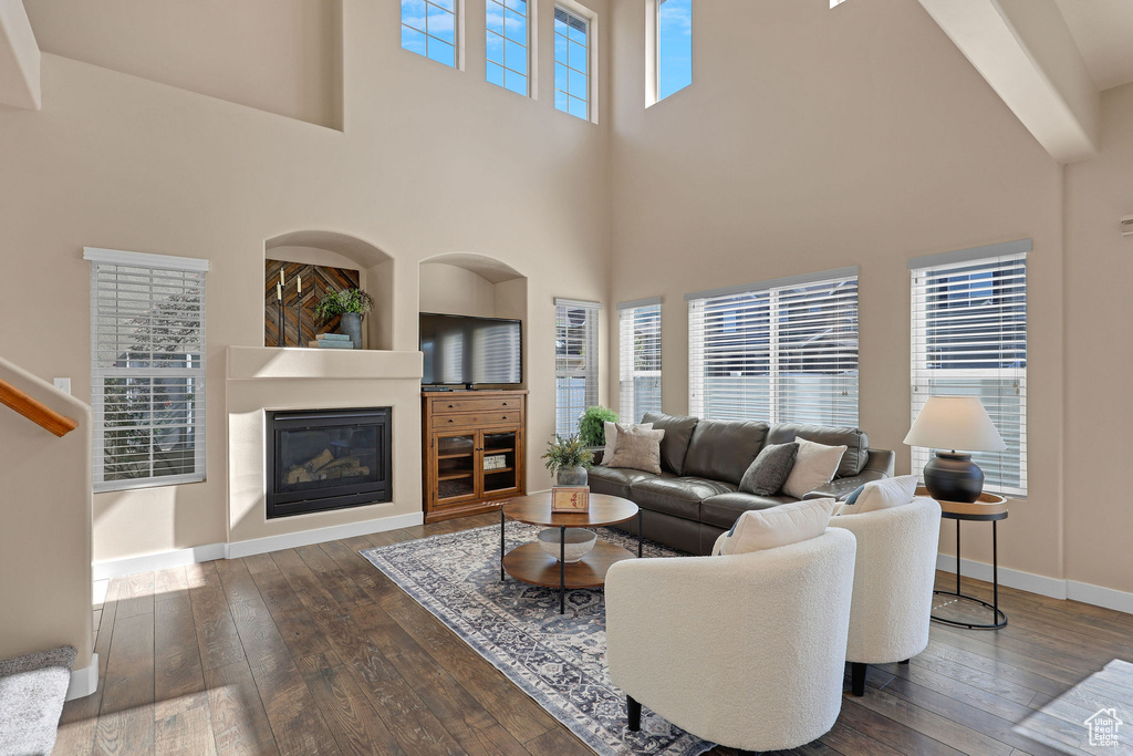 Living room with dark wood-style flooring, a towering ceiling, and a glass covered fireplace