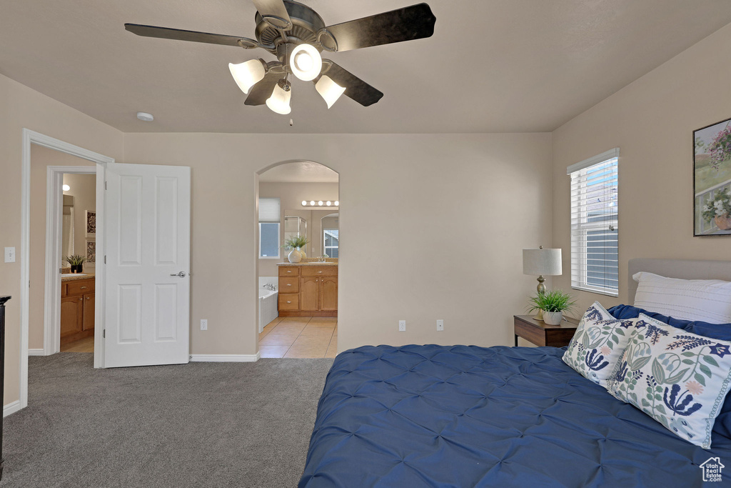 Bedroom with arched walkways, light carpet, ensuite bath, ceiling fan, and light tile patterned flooring