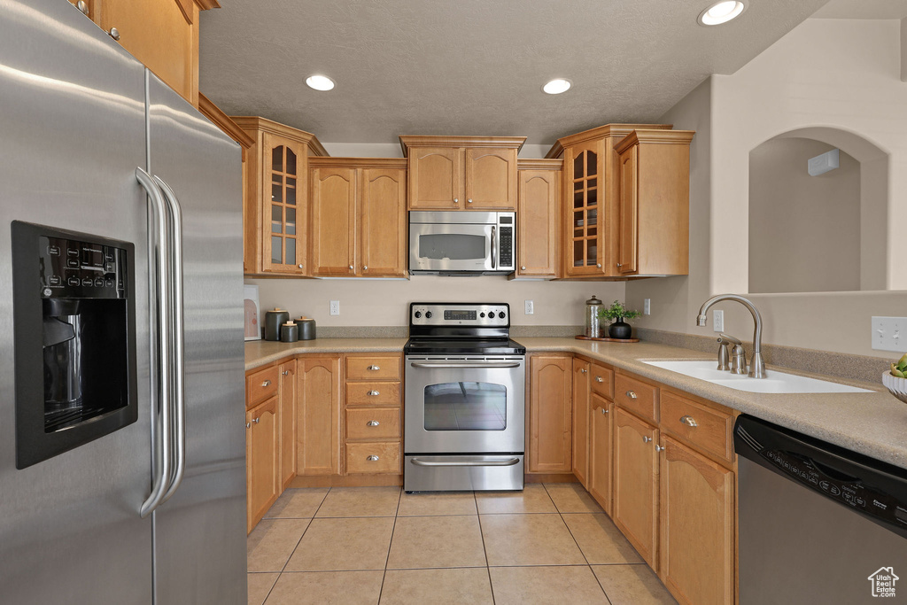 Kitchen featuring stainless steel appliances, light countertops, light tile patterned floors, glass insert cabinets, and recessed lighting