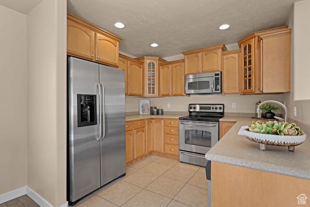 Kitchen featuring appliances with stainless steel finishes, recessed lighting, light countertops, light tile patterned flooring, and glass insert cabinets