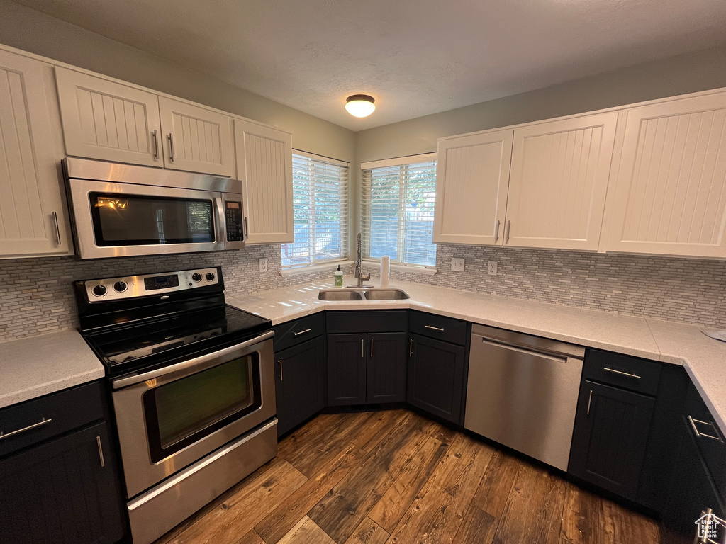 Kitchen with appliances with stainless steel finishes, white cabinets, dark cabinets, light countertops, and decorative backsplash