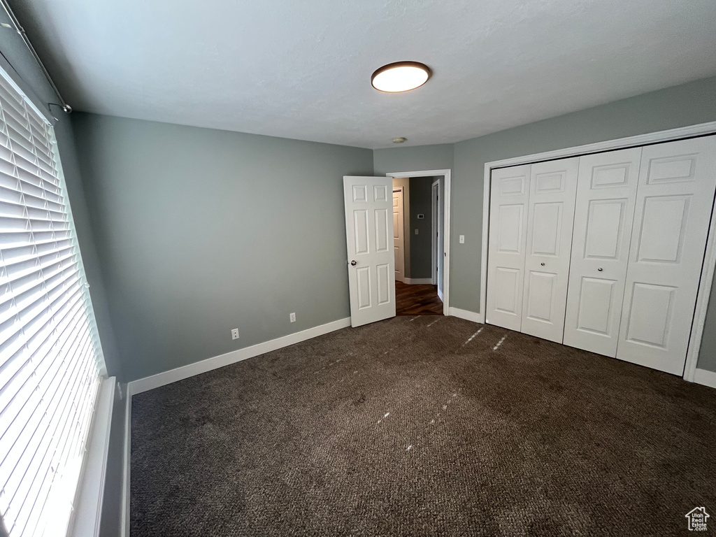 Unfurnished bedroom featuring dark colored carpet, multiple windows, and a closet