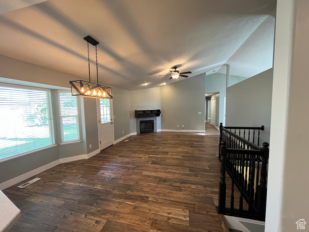Unfurnished living room with lofted ceiling, dark wood finished floors, a chandelier, a fireplace, and a ceiling fan
