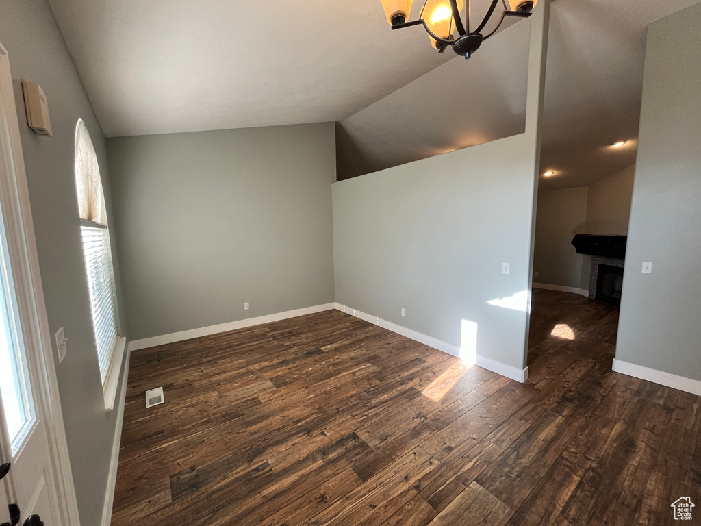 Unfurnished room with vaulted ceiling, dark wood-style floors, plenty of natural light, a chandelier, and a fireplace