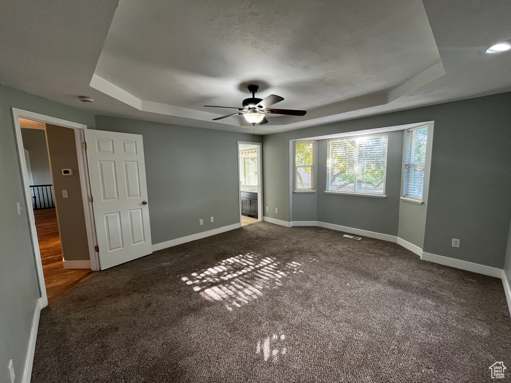 Unfurnished bedroom featuring a tray ceiling, carpet flooring, connected bathroom, and ceiling fan
