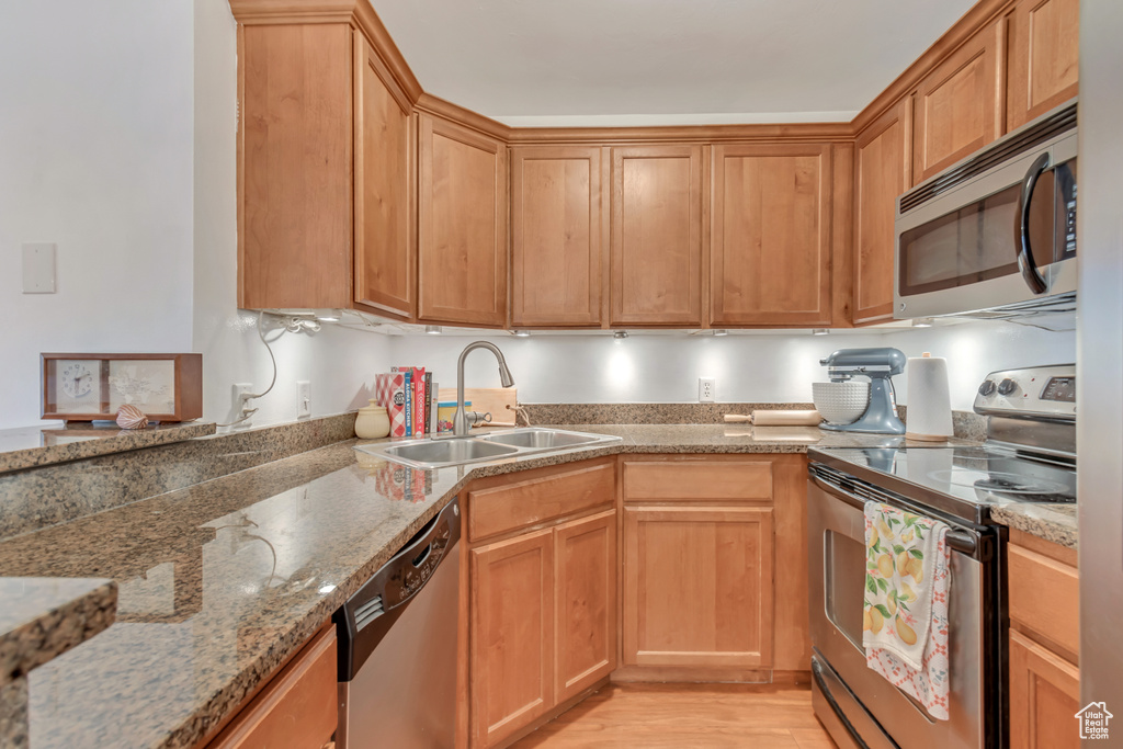 Kitchen with stainless steel appliances, light wood finished floors, and light stone countertops