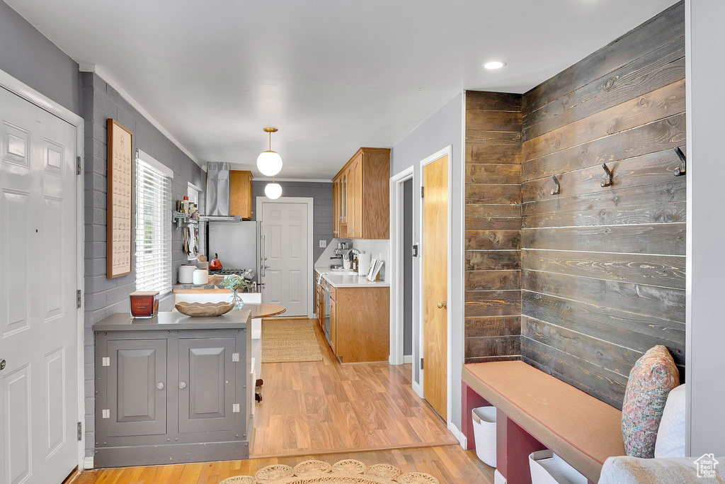 Kitchen featuring wall chimney range hood, light wood-type flooring, brown cabinets, light countertops, and wood walls
