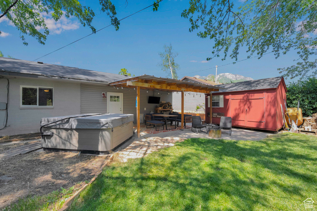Back of house featuring a hot tub, a patio area, a shed, a lawn, and a pergola