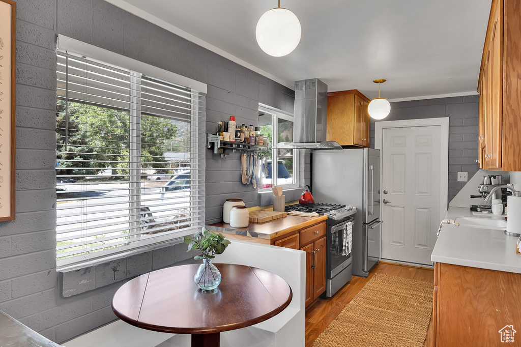 Kitchen featuring wall chimney exhaust hood, stainless steel appliances, light wood-type flooring, brown cabinets, and light countertops