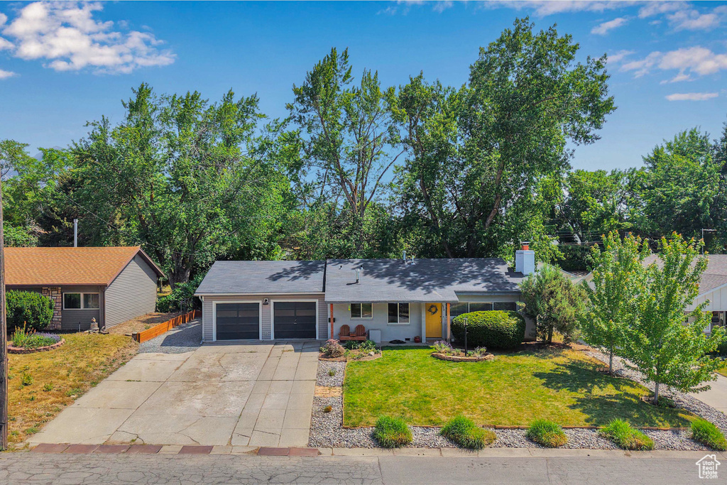 View of front facade featuring an attached garage, a front lawn, driveway, and a chimney