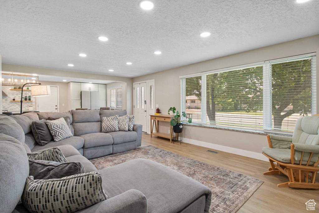 Living area with a chandelier, a textured ceiling, recessed lighting, and light wood-style flooring
