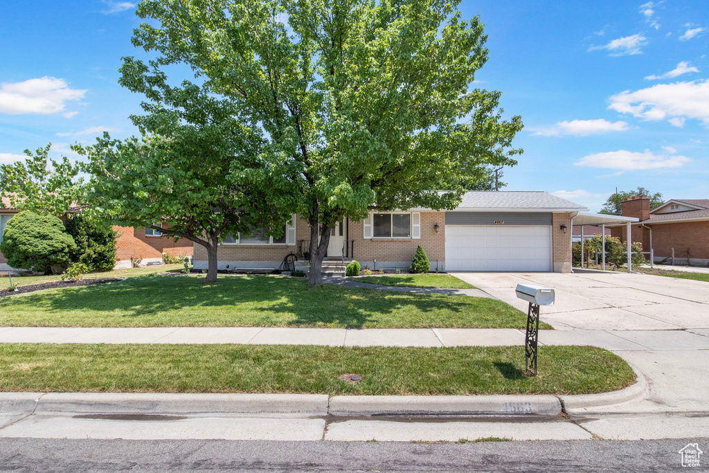Obstructed view of property with concrete driveway, brick siding, a garage, a front lawn, and a carport