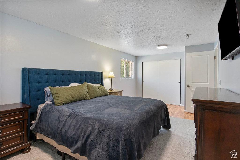 Bedroom with a closet, light wood-style floors, and a textured ceiling