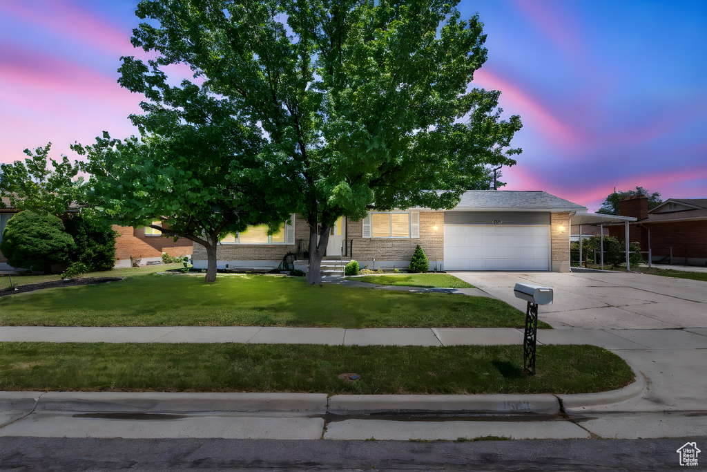 Obstructed view of property with an attached garage, driveway, brick siding, and a front lawn