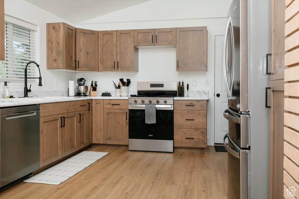 Kitchen with stainless steel appliances, light wood-style flooring, lofted ceiling, and light countertops