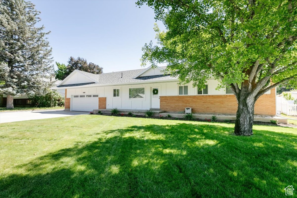 View of front of house with brick siding, board and batten siding, concrete driveway, an attached garage, and a front yard