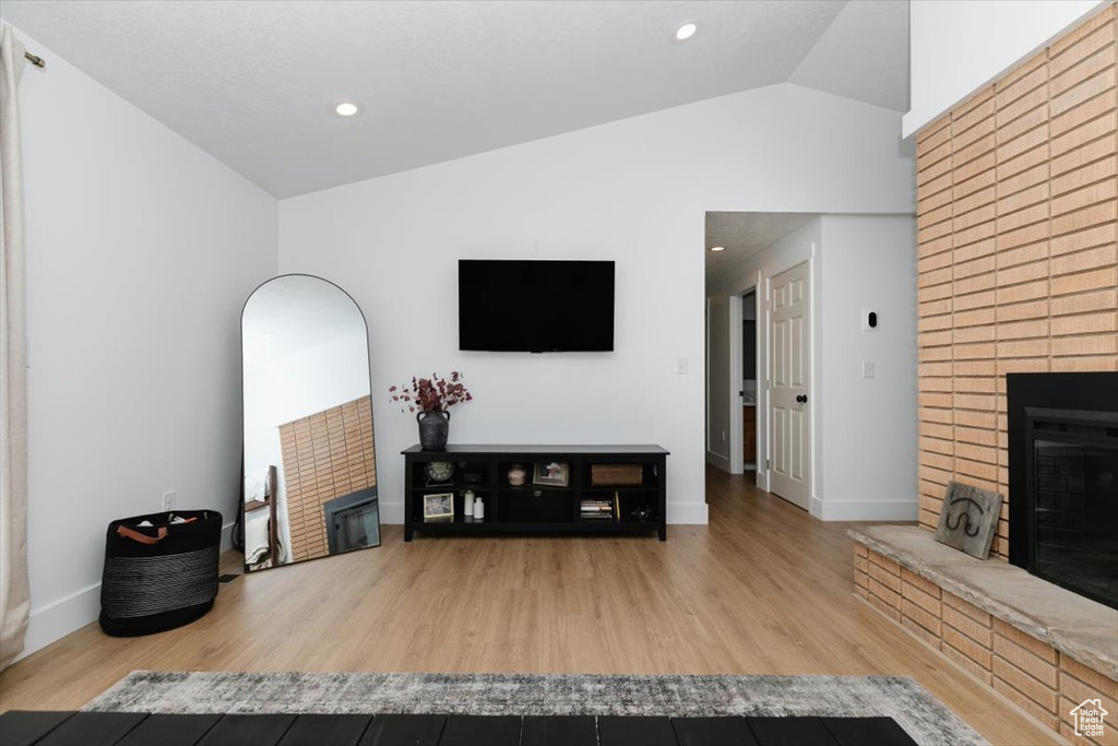 Living room with a fireplace, vaulted ceiling, wood finished floors, and recessed lighting
