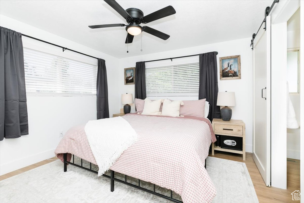 Bedroom featuring a barn door, light wood-style floors, and ceiling fan