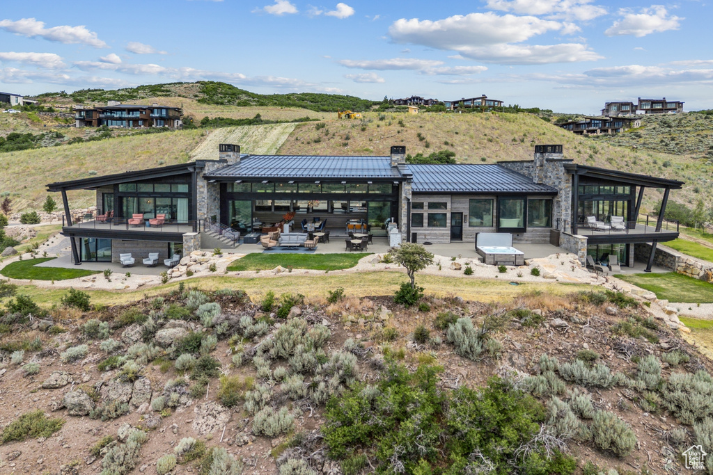 Back of house featuring a chimney, a standing seam roof, stone siding, a metal roof, and a patio area