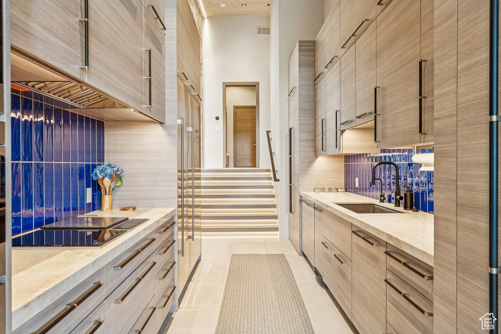Kitchen with modern cabinets, tasteful backsplash, a towering ceiling, light brown cabinets, and light tile patterned flooring