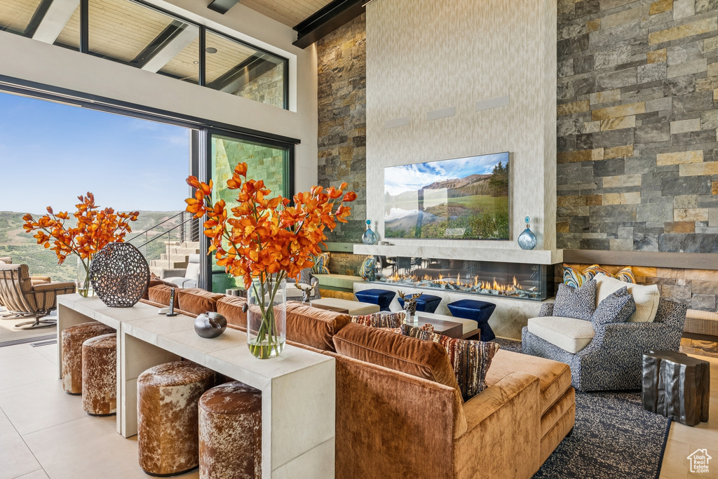 Tiled living area featuring a towering ceiling, a glass covered fireplace, and a wood ceiling with exposed beams