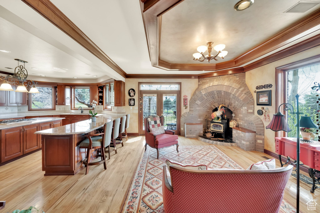 Living area with a tray ceiling, ornamental molding, a chandelier, a wood stove, and light wood-type flooring