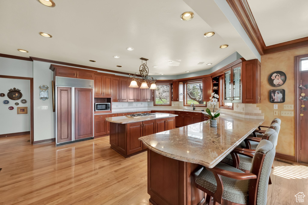 Kitchen featuring built in appliances, ornamental molding, light wood finished floors, tasteful backsplash, and a kitchen island