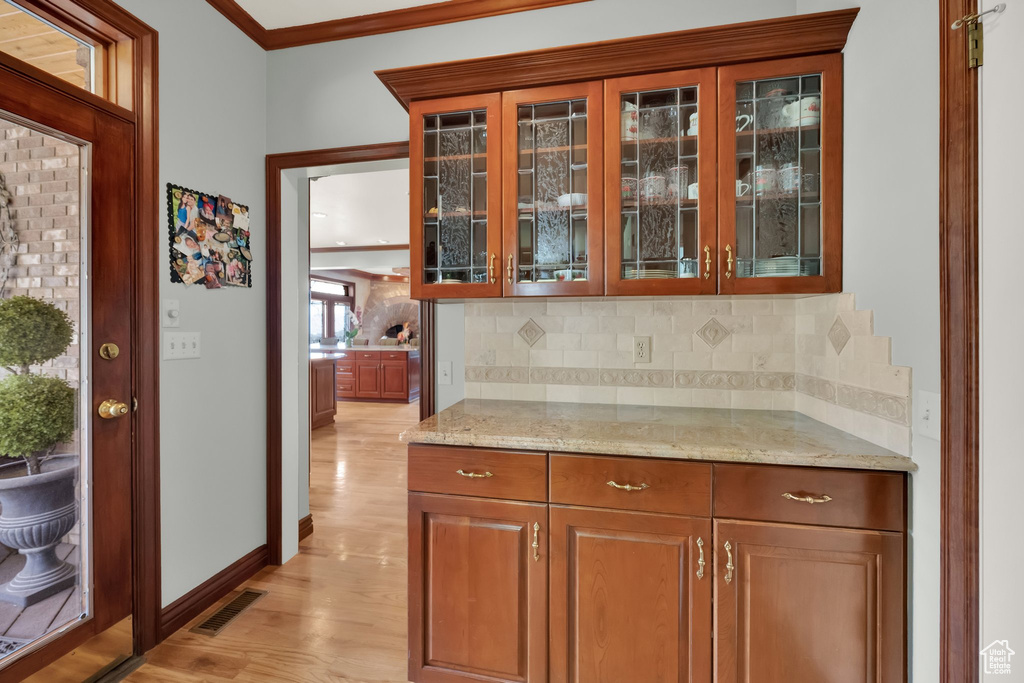 Bar area featuring light wood-style floors, backsplash, and ornamental molding