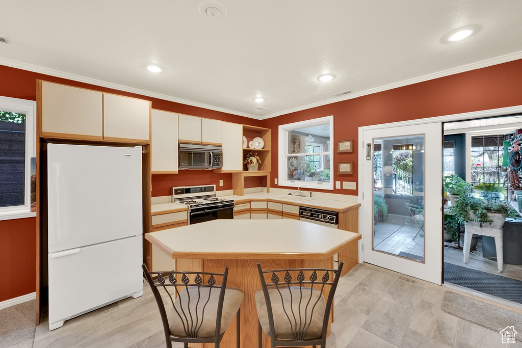 Kitchen featuring white appliances, light countertops, crown molding, open shelves, and a center island