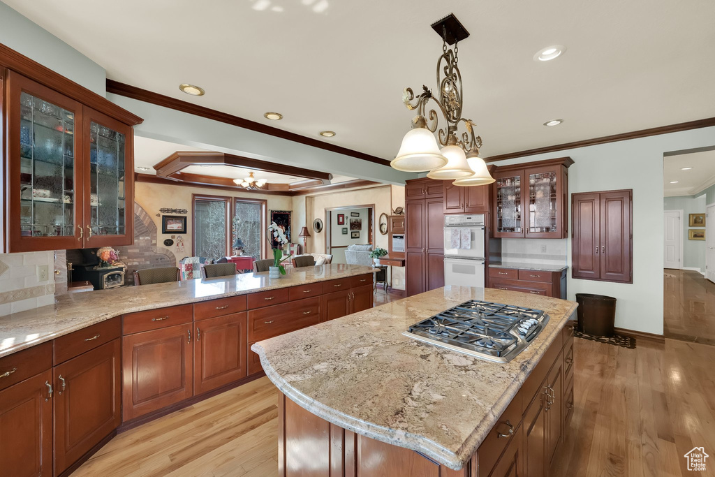 Kitchen with stainless steel gas stovetop, crown molding, a chandelier, light wood-style flooring, and white double oven