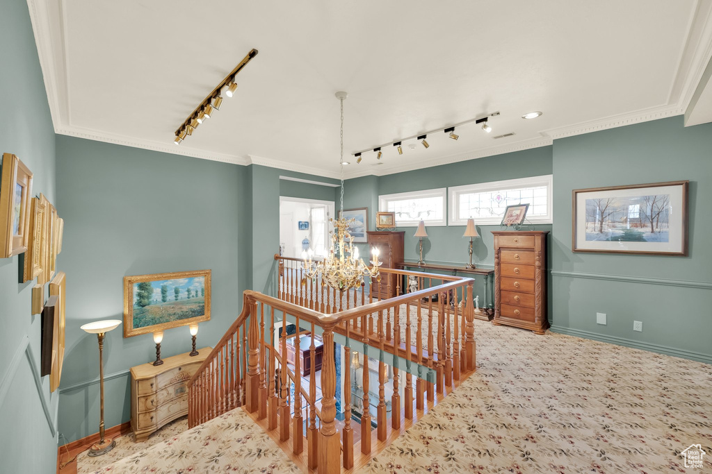 Stairway with rail lighting, a chandelier, ornamental molding, and carpet flooring
