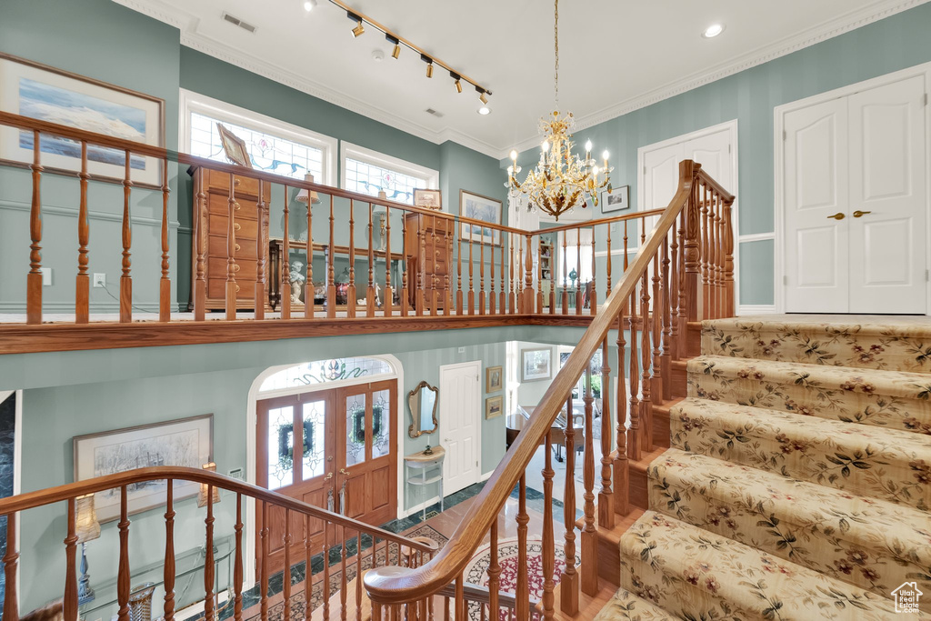Stairs featuring a chandelier, track lighting, ornamental molding, wood finished floors, and a high ceiling