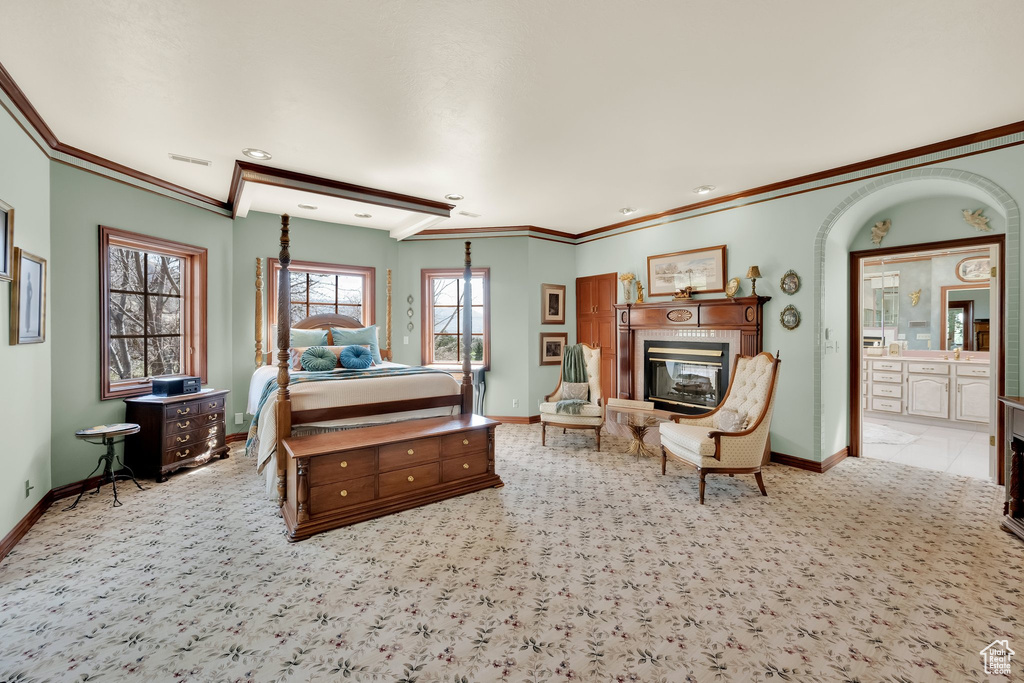 Carpeted bedroom featuring a glass covered fireplace, ornamental molding, and ensuite bathroom