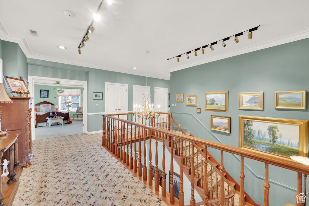 Hallway featuring rail lighting, a chandelier, ornamental molding, carpet, and an upstairs landing