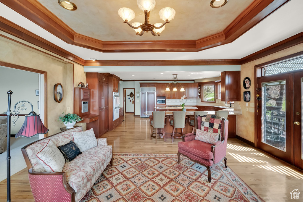 Living room featuring a chandelier, crown molding, a tray ceiling, light wood finished floors, and recessed lighting